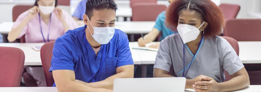 Two college students in library bump fists, face masks graduate silhouette 2019 2020