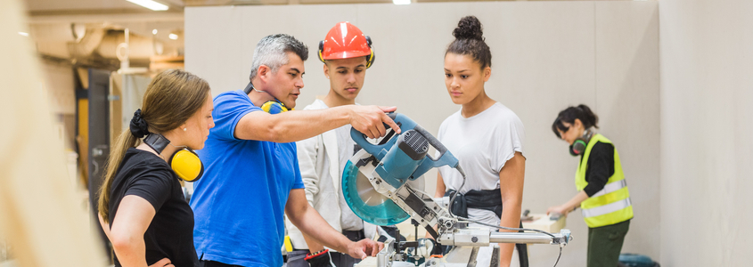 Trainees watching confident male carpenter cutting with electric saw in workshop Industry Credentials: a Valuable Student Pathway to Success